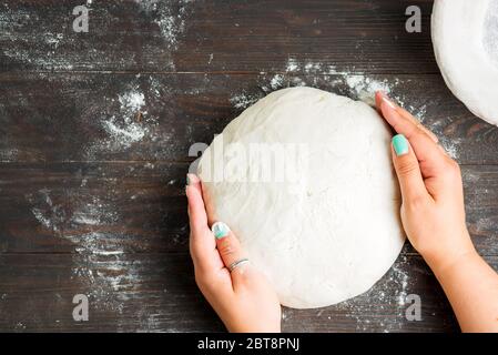 Frisch gekochter Teig und Schaber in der Hand einer Frau. Prozess der Vorbereitung von hausgemachtem Brot auf einem dunklen Holzhintergrund, kopieren Raum. Schritt für Schritt. Stockfoto