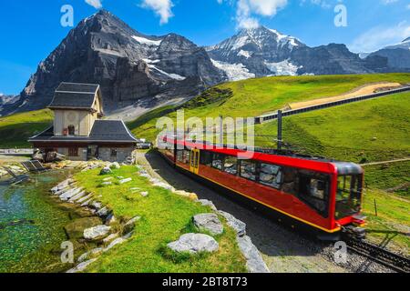 Moderner roter Personenzug in der Nähe der kleinen Bergkapelle. Zahnradbahn rot Touristenbahn von der Bergstation, Jungfraujoch, Berner OBE Stockfoto