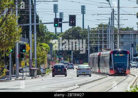 Verkehr und eine Sydney Light Rail Straßenbahn auf der Anzac Parade in Kensington, Sydney, Australien, mit den Lichtern des SCG (Sydney Cricket Ground) im Hintergrund. Stockfoto