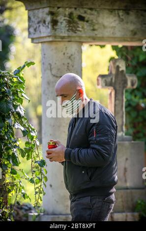 Auf dem Friedhof erinnert ein Mann an seinen verlorenen Verwandten, der eine Gesichtsmaske trägt, die durch den Virus Covid - 19 verursacht wurde. Stockfoto