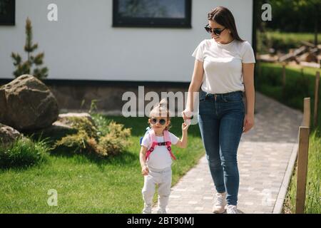 Mutter mit ihrem liebenswert kleine Tochter gehen vor Haus. Glückliche Familie verbrachte Zeit im Freien. Mutter und Tochter in Sonnenbrille Stockfoto
