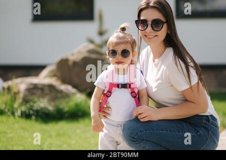 Mutter mit ihrem liebenswert kleine Tochter gehen vor Haus. Glückliche Familie verbrachte Zeit im Freien. Mutter und Tochter in Sonnenbrille Stockfoto