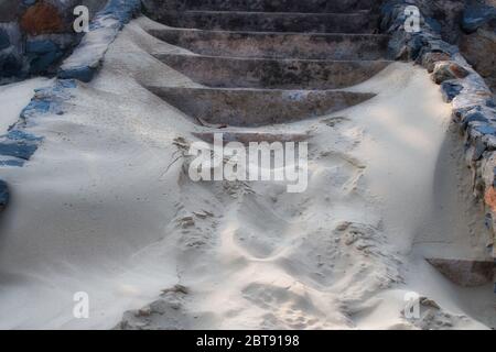 Dieses einzigartige Foto zeigt eine Steintreppe am Strand, die fast vollständig mit Sand bedeckt ist, der vom Wind geblasen wurde. Stockfoto