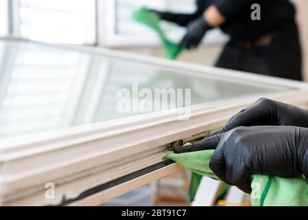 Zwei Gebäudemanagementreiniger reinigen ein Fenster und einen Fensterrahmen mit grünen Mikrofasertüchern Stockfoto