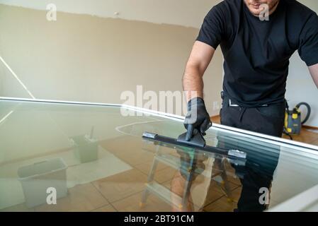 Ein professioneller Reiniger, der ein großes Fenster mit einem Abzieher und einem Schaber reinigt Stockfoto