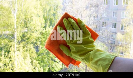 Eine Frau Hand in gelben Handschuhen mit einem orangefarbenen Lappen wäscht das Fenster. Frühjahrsputz, Hausarbeit Konzept. Stockfoto