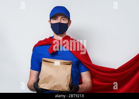 Kurier mit Tasche trägt medizinische Gesichtsmaske in Superhelden Mantel. Konzept der Superheldentum Kurier während Coronavirus Ausbruch. Stockfoto