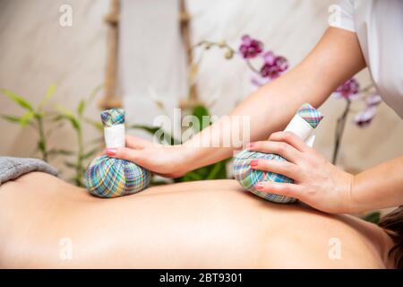 Ruhige junge Frau, die im Spa eine Massage mit Kräutersäcken genießt Stockfoto