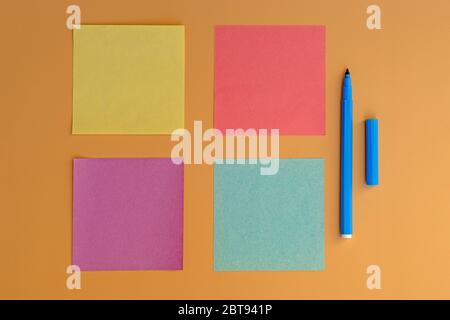 Faltblätter in verschiedenen Farben für Notizen und einen blauen Marker zum Schreiben. Aufkleber von gelb, grün, rosa Farbe von oben. Leere kleine quadratische Papier Notizen o Stockfoto