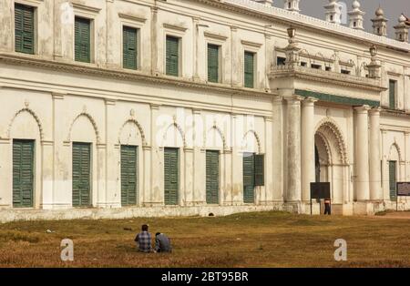 Murshidabad, Westbengalen/Indien - Januar 15 2018: Zwei Personen sitzen auf den Gärten vor der imposanten Außenfassade des Nizamat Imambara. Stockfoto