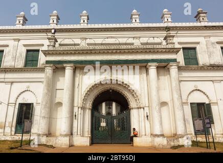 Murshidabad, Westbengalen/Indien - Januar 15 2018: Ein Hausmeister sitzt auf einem Regal außerhalb der Außenfassade und Tür von Nizamat Imambara. Stockfoto