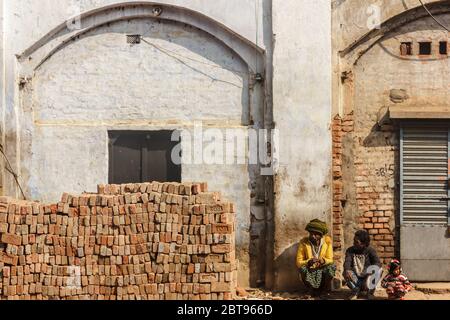 Murshidabad, Westbengalen/Indien - Januar 17 2018: Zwei Männer und ein Junge sitzen neben einem Ziegelhaufen unter den gewölbten Wänden eines Gebäudes. Stockfoto