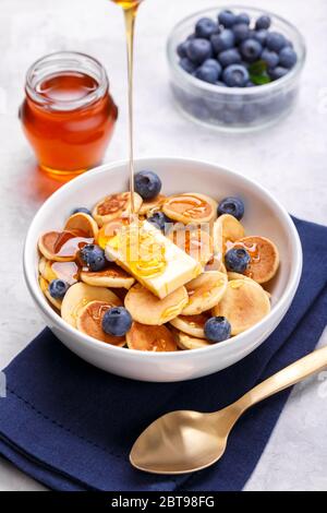Hausgemachte trendige Müsli Mini Pfannkuchen mit Honig und Heidelbeeren auf grauem Stein Hintergrund, Nahaufnahme, vertikal Stockfoto