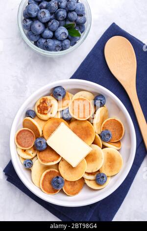 Hausgemachte trendige Müsli Mini Pfannkuchen mit Honig und Heidelbeeren auf grauem Stein Hintergrund, Nahaufnahme, vertikal Stockfoto