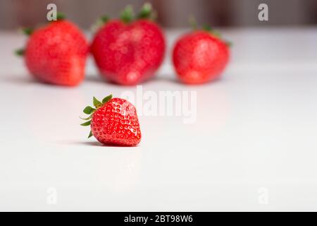 Eine Nahaufnahme einer kleinen Erdbeere und im verschwommenen Hintergrund drei große Erdbeeren Stockfoto