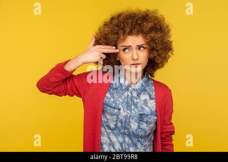 Ich möchte mich selbst töten. Porträt einer depressiven Frau mit lockigen Haaren, die auf die Fingerpistole und den Schießkopf zeigt, verzweifelt, über Selbstmord nachdenkend. Stockfoto