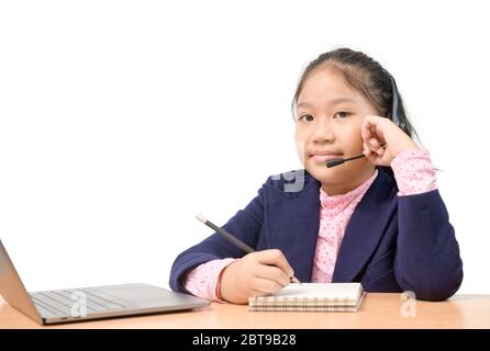 Nette asiatische Schulmädchen trägt ein Headset und Hausaufgaben zu tun, beobachten Lehrer online unterrichten über Laptop aufgrund des Ausbruchs der Koronarvirus oder Cov Stockfoto