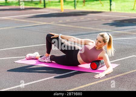 Motivierte sportliche Frau Training auf Matte Outdoor Sommertag, mit Schaum Roller Massagegerät zur Entspannung, Dehnung der Wirbelsäule Muskeln, Faszien Übung Stockfoto