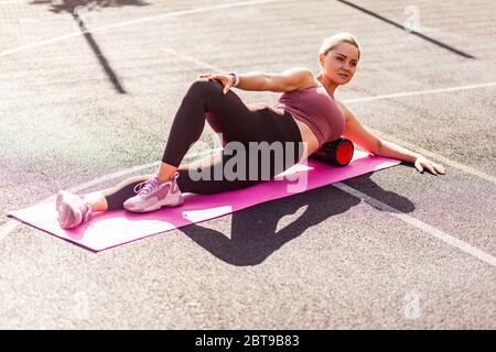 Motivierte sportliche Frau Training auf Matte Outdoor Sommertag, mit Schaum Roller Massagegerät zur Entspannung, Dehnung der Wirbelsäule Muskeln, Faszien Übung Stockfoto