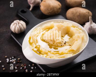 Kartoffelpüree mit Gewürzen und Olivenöl in weiße Schüssel am schwarzen Brett über dunkle konkreten Hintergrund Stockfoto