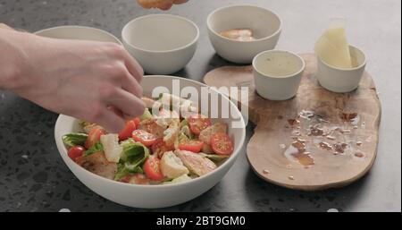 Man Hand fügen Croutons auf caesar Salat in weißer Keramik Schüssel auf Betonplatte Stockfoto