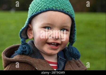 Entzückender einjähriger kleiner Junge grinst frech und aufgeregt, draußen herumlaufen zu können: Sheffield Park, East Sussex, England, Großbritannien. MODELL FREIGEGEBEN Stockfoto