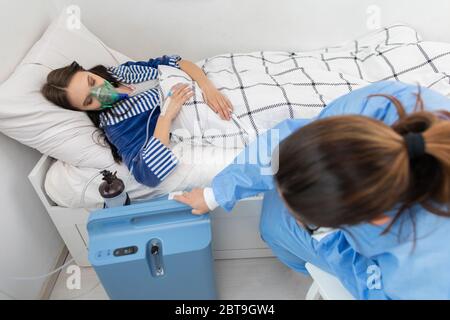 Der Teenager hat einen Ventilator angeschlossen. Der Arzt passt die Atemschutzmaske an, um die richtige Sauerstoffdosis zu geben. Stockfoto