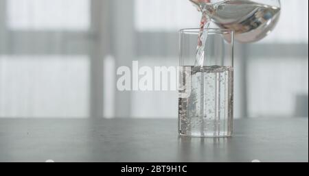 In Zeitlupe Wasser in das Becherglas auf die Arbeitsplatte aus Beton gießen Mit Fenster im Hintergrund Stockfoto