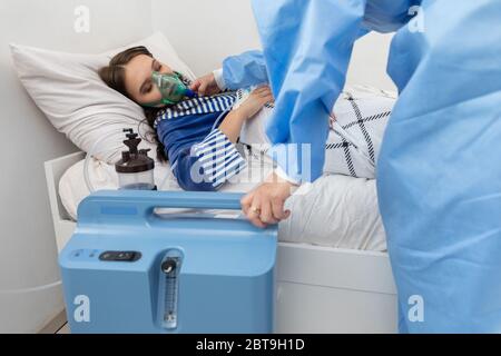 Der Teenager hat einen Ventilator angeschlossen. Der Arzt passt die Atemschutzmaske an, um die richtige Sauerstoffdosis zu geben. Stockfoto