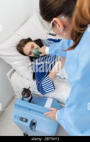 Der Teenager hat einen Ventilator angeschlossen. Der Arzt passt die Atemschutzmaske an, um die richtige Sauerstoffdosis zu geben. Stockfoto