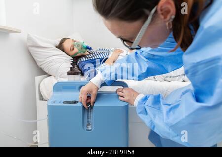 Der Teenager hat einen Ventilator angeschlossen. Der Arzt passt die Atemschutzmaske an, um die richtige Sauerstoffdosis zu geben. Stockfoto