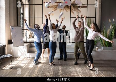 Begeisterte verschiedene Geschäftsleute, die Papiere werfen und den Erfolg von Teamarbeit feiern Stockfoto