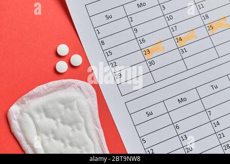 Frauen Tampon auf rotem Hintergrund mit einem Kalender und Hormonpillen. Draufsicht. Stockfoto