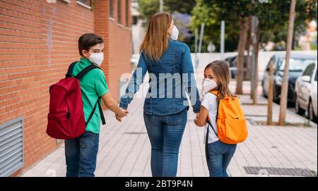 Mutter mit ihren Kindern gehen mit Masken in die Schule bei einer Coronavirus-Pandemie Stockfoto