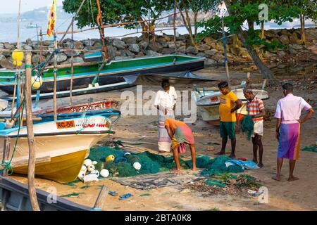 Fischer pflegen ihre Netze mit ihren Booten am Strand außerhalb von Galle Stockfoto
