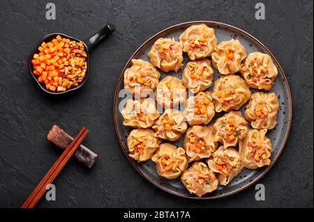 Shumai oder Kanom Jeeb oder gedämpfte Schweinefleisch- und Garnelenknödel auf einem schwarzen Teller auf dunklem Schieferhintergrund. Shumai ist ein chinesisches Gericht mit Hackfleisch m Stockfoto