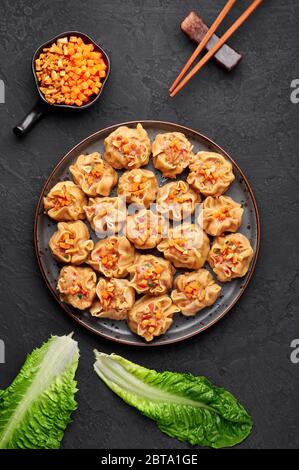 Shumai oder Kanom Jeeb oder gedämpfte Schweinefleisch- und Garnelenknödel auf einem schwarzen Teller auf dunklem Schieferhintergrund. Shumai ist ein chinesisches Gericht mit Hackfleisch m Stockfoto