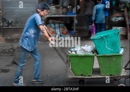 Der junge Inder schiebt in einer armen Gegend von ​​Mumbay einen alten Wagen mit Eimern Müll vor sich Stockfoto