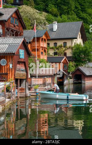 Mann, der ein kleines Motorboot zum Mieten aus einem Holzboothaus in Hallstatt, Salzkammergut, OÖ, Österreich, begibt Stockfoto