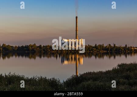 Alte Müllverbrennungsanlage am Ufer des Sees. Alte Müllverbrennungsanlage mit Rauchschornstein. Farbenfroher Himmel im Hintergrund Stockfoto