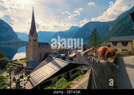 Weibliche Touristen betrachten die atemberaubende Hallstatt, Salzkammergut Region, OÖ, Österreich, von einem erhöhten Aussichtspunkt über den Dächern des berühmten Dorfes Stockfoto