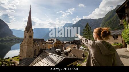 Weibliche Touristen zeigen auf atemberaubende Hallstatt, Salzkammergut Region, OÖ, Österreich, von einem erhöhten Aussichtspunkt über den Dächern des berühmten Dorfes Stockfoto