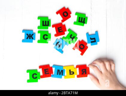 Auf weißem Hintergrund liegen die Buchstaben des russischen Alphabets. Das Kind legte die Inschrift der Familie auf Russisch aus. Stockfoto