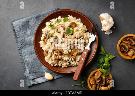 Ein Gericht der italienischen Küche - Risotto aus Reis und Pilzen in einem braunen Teller auf schwarzem Schiefergrund. Ansicht über dem Bild. Stockfoto