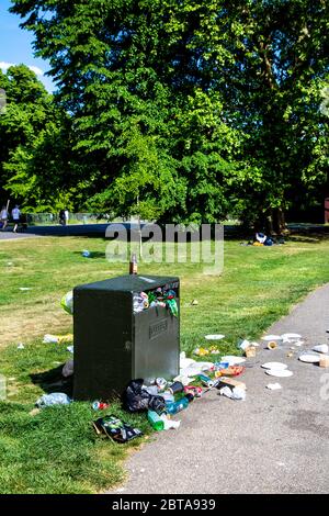 Ein Mülltonne in einem Park, der überfüllt und voller Müll ist, Müll auf dem Rasen und auf dem Weg verstreut (Battersea Park, London, UK) Stockfoto