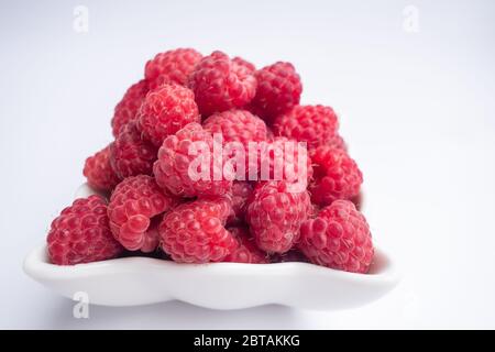 Himbeerbeeren Nahaufnahme. Frische Himbeeren in einer weißen Tasse auf weißem Hintergrund. Weichstellung. Stockfoto