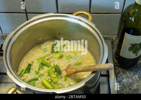 Risotto Reis mit Spargel, Zwiebeln und Weißwein kochen. Holzlöffel in der Pfanne mit Reis. Hohe Winkelansicht. Stockfoto