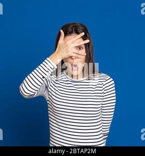 Brünette junge Frau trägt ein gestreiftes T-Shirt auf blauem Hintergrund Stockfoto