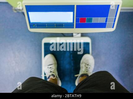 Ein junger Mann steht auf der Waage in der Turnhalle. Stockfoto