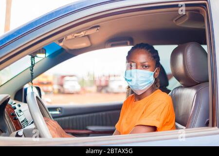 Junge schöne afrikanische Dame in einem Fahrzeug trägt Gesichtsmaske zu verhindern, zu verhindern, verhindert, sich von dem Ausbruch in der Gesellschaft Stockfoto